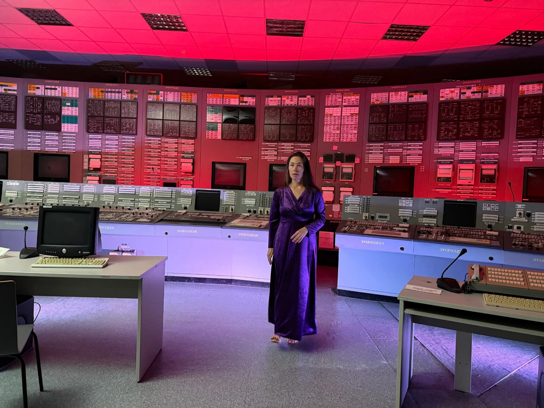 Film Camp performer in a purple dress standing in a control room under red lighting
