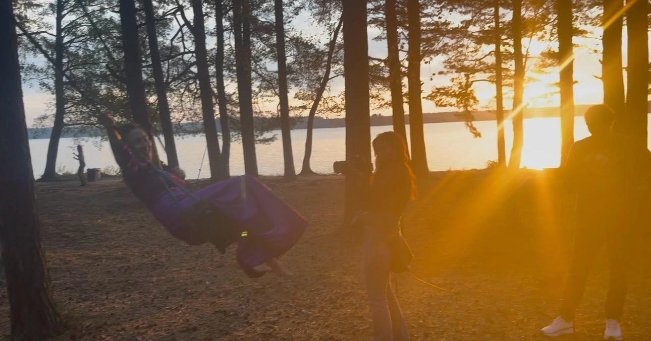 Film Camp crew filming a performer on a swing beside the lake at sunset